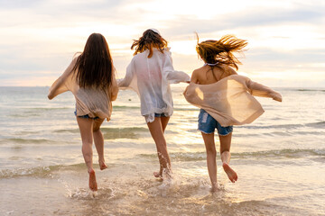 Wall Mural - Group of Young Asian woman friends walking and playing together in the sea at tropical island beach at summer sunset. Attractive girl enjoy and fun outdoor lifestyle travel nature on holiday vacation.
