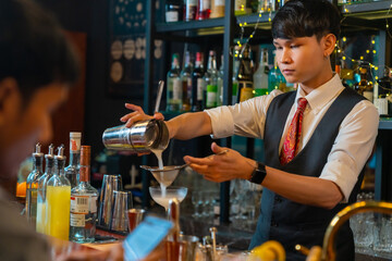 Professional Asian man bartender preparing and serving cocktail drink to customer on bar counter at nightclub. Barman making mixed alcoholic drink for celebrating holiday party at restaurant bar.