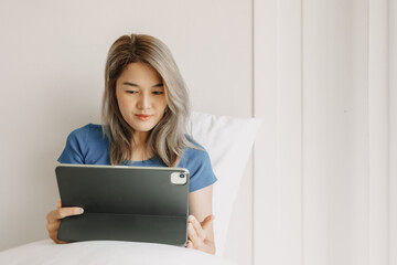 Wall Mural - Happy freelance asian woman work on tablet on the hotel bed on travel trip.