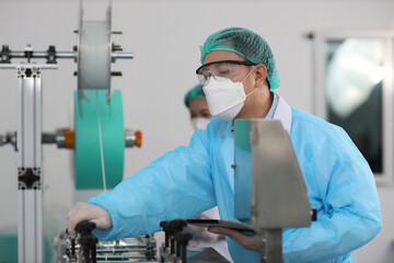 Canvas Print - Worker in personal protective equipment or PPE inspecting quality of mask and medical face mask production line in factory, manufacturing industry and factory concept.