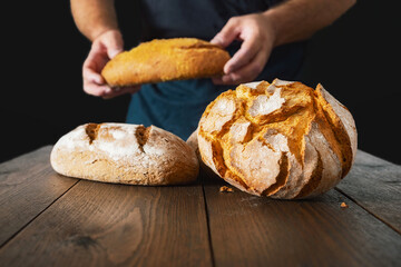 Aufkleber - Whole fresh loaves of bread on wooden table on black background in the background man baker holds bread