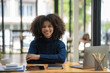 © Songsak C - Young African American businesswoman smiling confidently while sitting with her arms crossed at her office desk.