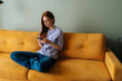 © dikushin - Portrait of frustrated young woman sitting on yellow couch looking at smartphone screen thinking about problem difficulty, feeling failure and exhausted, suffering grief and bad relationship