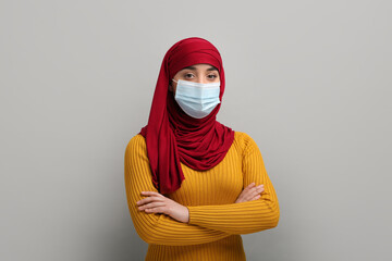 Wall Mural - Portrait of Muslim woman in hijab and medical mask on light gray background