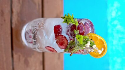 Wall Mural - Mojito cocktail glass with ice and cherry and mint, soda and gin near a blue pool close up