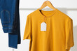 Yellow t shirt with tag and denim trousers on clothes rail with copy space on white background