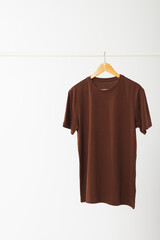 Brown t shirt on hanger hanging from clothes rail with copy space on white background