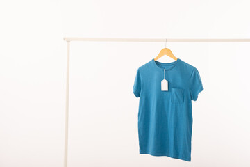 Wall Mural - Blue t shirt with tag on hanger hanging from clothes rail with copy space on white background