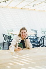 Wall Mural - Happy woman sitting at outdoor cafe table and talking on phone with cup of coffee, smiling woman enjoying telecommuting in cafe or studying online