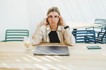 Wall Mural - Young happy woman sitting at outdoor cafe table and talking on phone with cup of coffee, smiling woman enjoying telecommuting in cafe or studying online on laptop