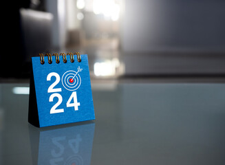 Wall Mural - Happy new year 2024 banner background. 2024 numbers year with target icon on blue small desk calendar cover standing on glass table in office with copy space. Business goals and success concepts.