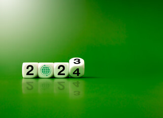 Wall Mural - 2024 happy new year with the green recycling, save planet and earth eco environment concepts. Flipping 2023 to 2024 year number with earth revolves icon on white blocks isolated on green background.