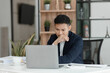 © SOMKID - sad asian businessman sitting at desk in modern office, stressed man, problem, Worried young man businessman,