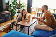 Smiling man holding coffee and playing wood blocks game with girlfriend near border collie at home