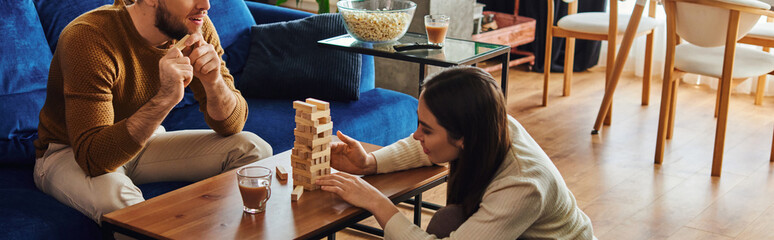 Wall Mural - Woman playing wood blocks game with boyfriend near popcorn and coffee at home, banner