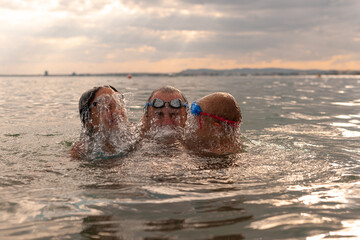 A father with his children emerges from the water. Everyone is wearing water goggles