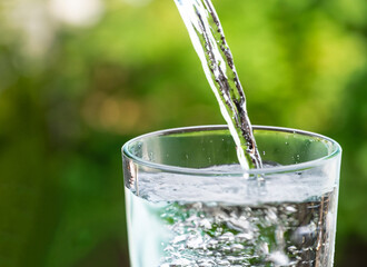 closeup water pouring into glass on green blurred background