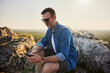 © baranq - Adult man using his phone sitting on the rock while hiking in Jura, Poland