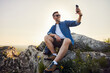 © baranq - Happy adult man taking selfie sitting on top of the mountain while hiking