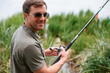 Positive and handsome man in sunglasses is fishing outdoors