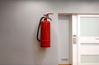 Red fire extinguisher on a gray wall with a white door and an outlet