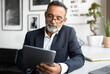 © Prostock-studio - Serious handsome caucasian senior businessman in suit and glasses uses tablet in modern office