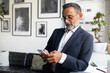 © Prostock-studio - Positive handsome caucasian senior businessman in suit and glasses typing on smartphone