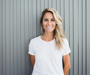 Blonde 40 year old woman in white t-shirt standing in front of a timber clad wall.