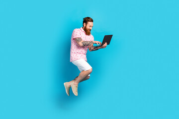 Full length profile portrait of crazy energetic guy jump running use wireless netbook isolated on blue color background