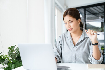 Poster - Confident young woman in smart casual wear working on laptop sitting near window in office or cafe. Concentrated at work.