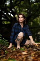 Poster - Young female with tattoos wearing a blue plaid shirt seated in a field of vibrant green grass