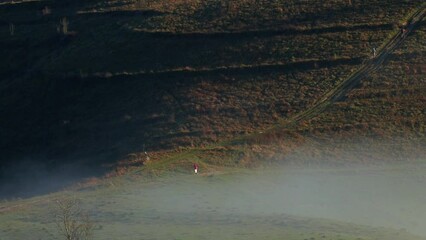 Wall Mural - Man walking on large green plains under valley hills with hazy sky on the horizon