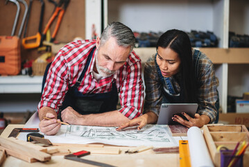 Wall Mural - Small business furniture owner and professional architect interior designer working in carpenter workshop with blueprint and tablet discussing about home furnishing design project.