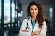 © sirisakboakaew - Smiling female doctor in a lab coat with arms crossed against