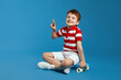 © Davidovici - Excited little boy in trendy red striped polo shirt smiling and showing peace gesture while sitting on modern skateboard against blue background