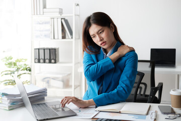 Businesswoman suffering shoulder pain sitting in a chair while working with a desktop computer.