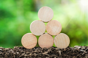 6 empty round wooden blocks on soil ground with green natural background and blur for own customer text or letters. Idea of environment, energy or business concept. Front view, banner copy space.