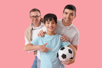 Wall Mural - Happy little boy with his dad and grandfather pointing at soccer ball on pink background