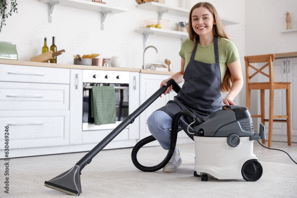 Young woman vacuuming carpet in kitchen