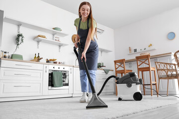 Canvas Print - Young woman vacuuming carpet in kitchen