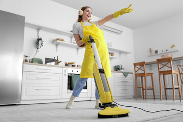 Canvas Print - Young woman with headphones hoovering carpet in kitchen