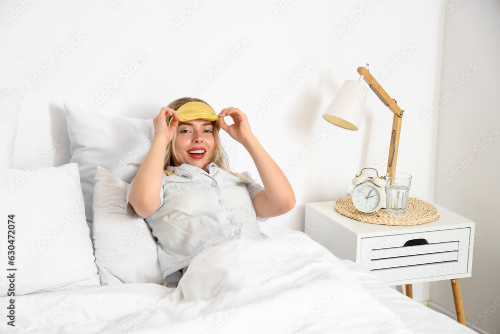 Young woman with sleeping mask lying in bed