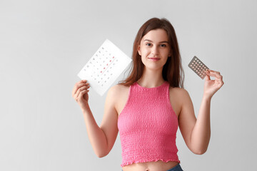 Canvas Print - Young woman with contraceptive pills and menstrual calendar on light background