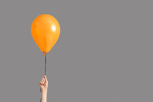 Female Hand With Orange Halloween Balloon On Grey Background