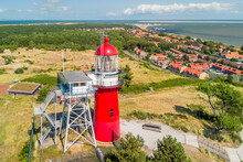 Aerial Drone Image Of The Island Vlieland. With Bright Red Lighthouse On Top Of A Sand Dune Overlooking The Small Town, Terschelling, The North Sea And The Wadden Sea. Blue Sky, Summer And Red Roofs