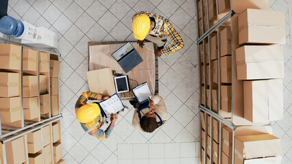 Team of people organizing supplies on racks and shelves, planning order production for retail store distribution. Colleagues working with merchandise and goods containers. Drone view.