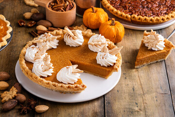 Traditional pumpkin pie topped with whipped cream with a slice taken out