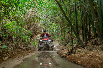 Poster - Asian guy having fun while driving an atv in the jungle alone. Drive through water in the deep forest.