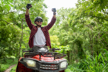 Wall Mural - Asian guy having fun while driving an atv in the jungle alone. Raised hands, smiling and happy.