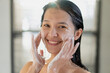 Asian woman in bathroom using sort of facial wash